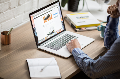 a person works on a laptop with a list and book sitting alongside.