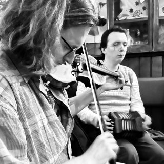 A young man playing fiddle and a young man playing concertina.