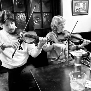 Two fiddlers playing side by side at a pub table.