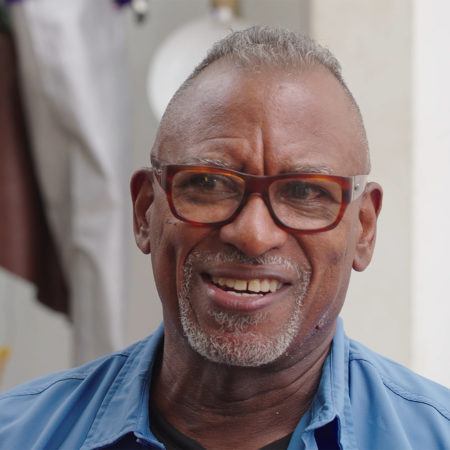 Daniel Lind-Ramso wearing glasses and a blue collared shirt, smiling out past the camera.