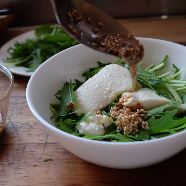 水菜に豆腐をスプーンですくって盛、ドレッシングをかけてるところ