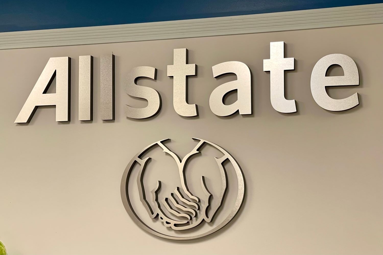 The side of a tan building showing Allstate's name and logo, a circle around two cupped hands.