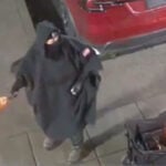 A masked figure allegedly holding a Molotov cocktail at a Tesla dealership in Salem, Oregon, in surveillance video.