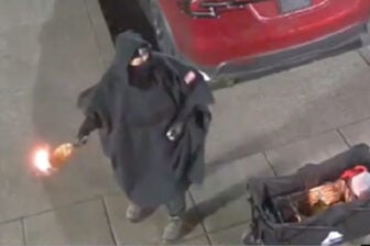 A masked figure allegedly holding a Molotov cocktail at a Tesla dealership in Salem, Oregon, in surveillance video.