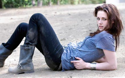 High-definition desktop wallpaper featuring a relaxed Kristen Stewart wearing boots and jeans, laying on the ground in an outdoor setting.