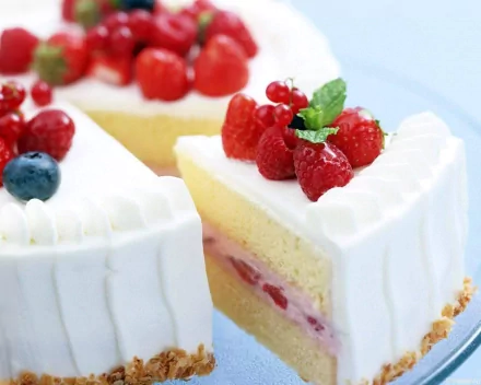 HD desktop wallpaper of a delicious cake adorned with fresh raspberries, blueberries, and currants, featuring creamy white frosting and a generous slice revealing a berry-filled layer.