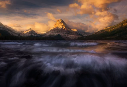 HD desktop wallpaper featuring a majestic mountain peak towering over a flowing river, surrounded by dramatic clouds and natural wilderness.