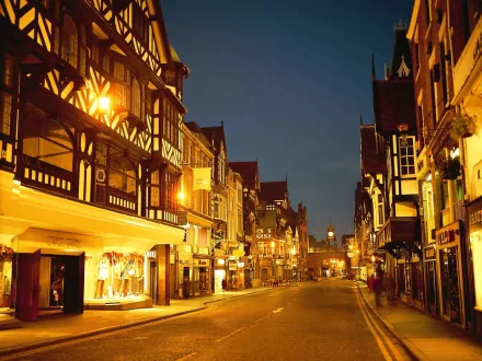 Night view of a man-made city street in Chester, England, featuring illuminated historic timber-framed buildings and a clear evening sky.
