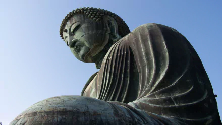 Close-up of a religious Buddha statue gazing downward against a clear sky — 2K Quad HD PC desktop wallpaper and background.