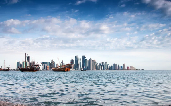 HD desktop wallpaper showing a scenic view of Doha's skyline from across the water, with traditional dhows floating in the foreground under a partly cloudy sky.