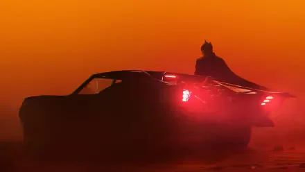 Silhouette of Batman standing near a sleek car with glowing taillights against a vibrant orange sky, captured in 4K Ultra HD for a dramatic PC desktop wallpaper.