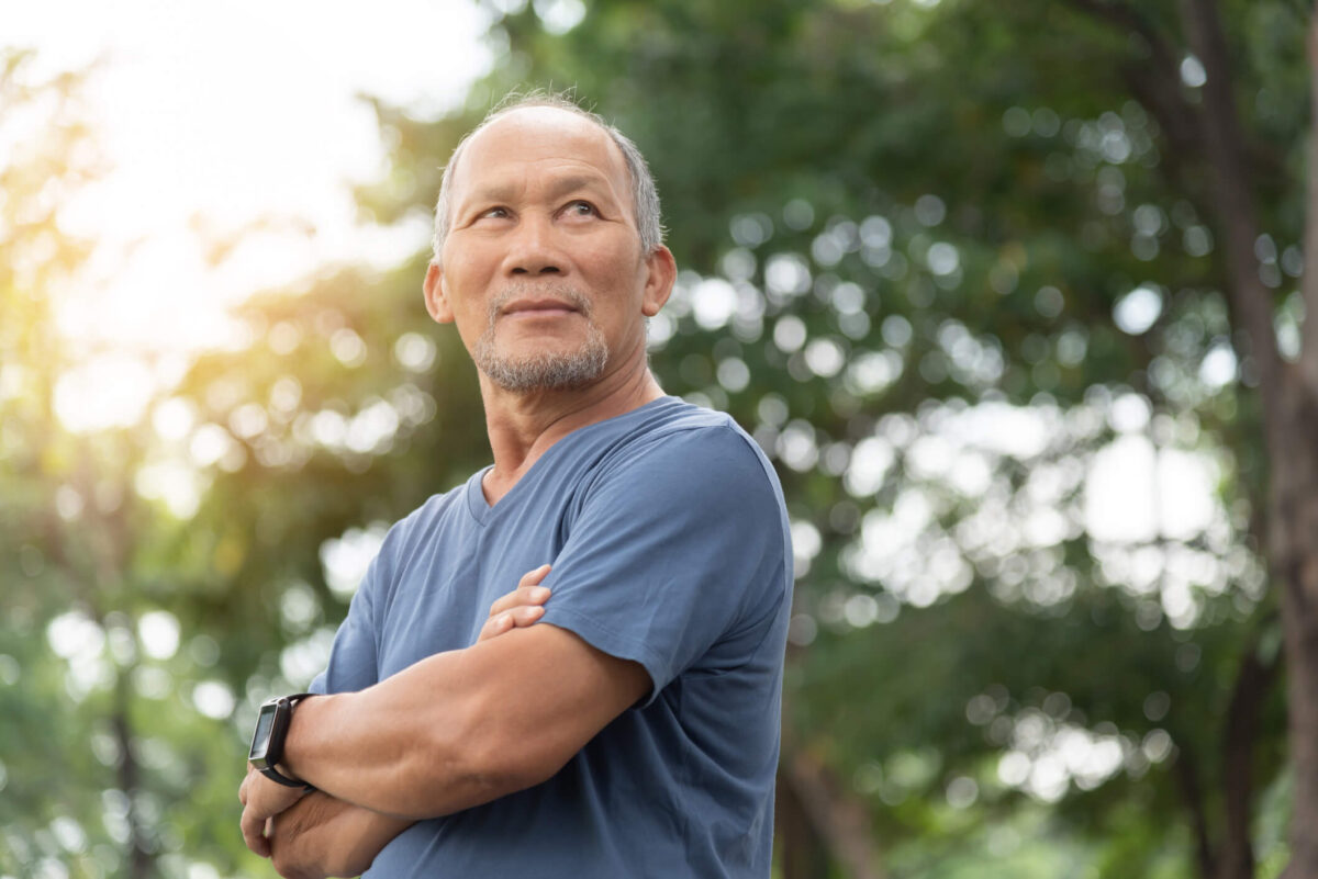 Man stands outdoors in front of trees in the sunshine.