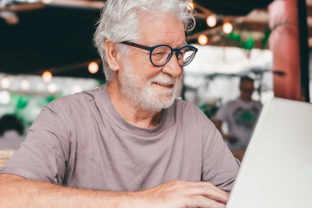 Man sitting in a cafe smiling while using laptop.