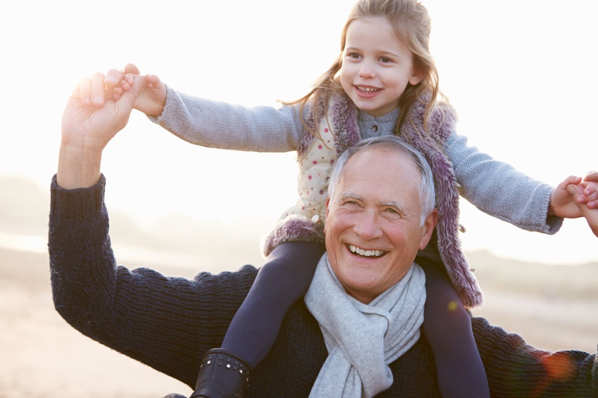 Grandfather smiling with his granddaughter on his shoulders.