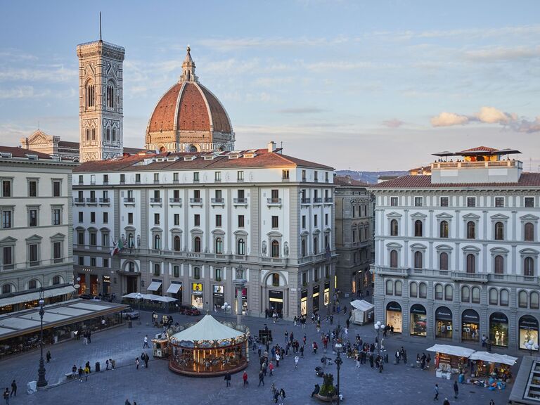 Stunning view of the Savoy Hotel exterior with a lively plaza in the foreground and a view of the Duomo in the background. 