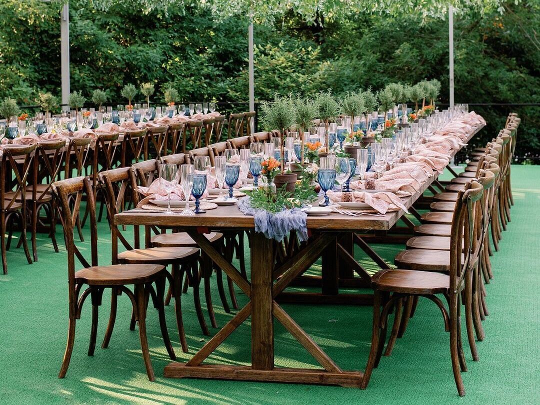 long wooden table with wooden cross back chairs and blue water goblets lining the table