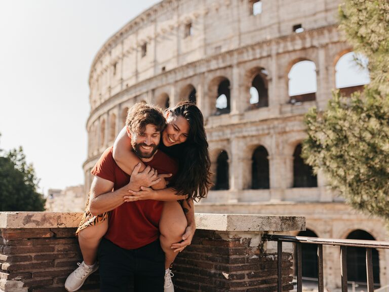 Bearded man giving girlfriend piggyback ride standing by Colosseum in Rome