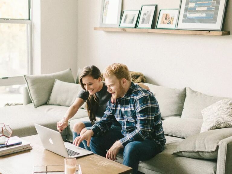 Engaged couple learning when to start their wedding registry on laptop