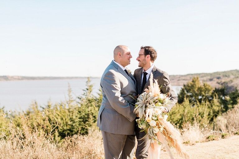 LGBTQ+ couple embracing on rustic lakeside overlook