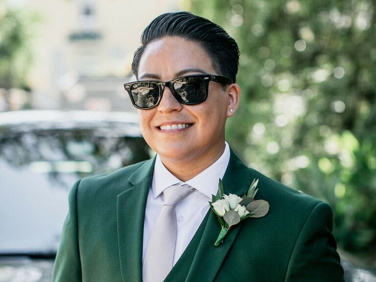 Bride wears a green suit and their hair in a short and sleek pompadour. 