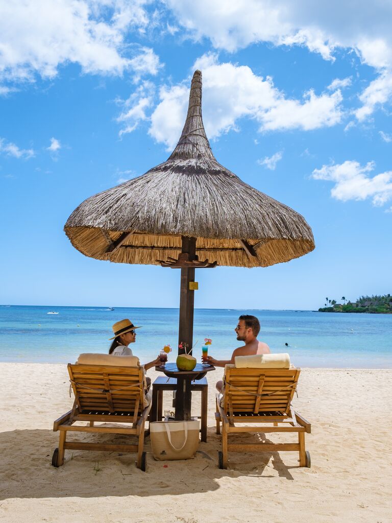 Couple sitting under umbrella on beach honeymoon