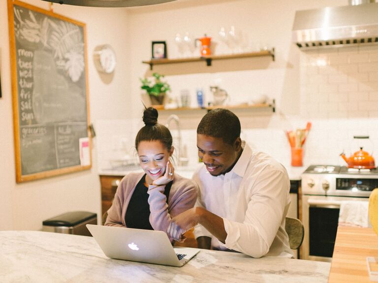 Engaged couple registering for gift cards on laptop at home