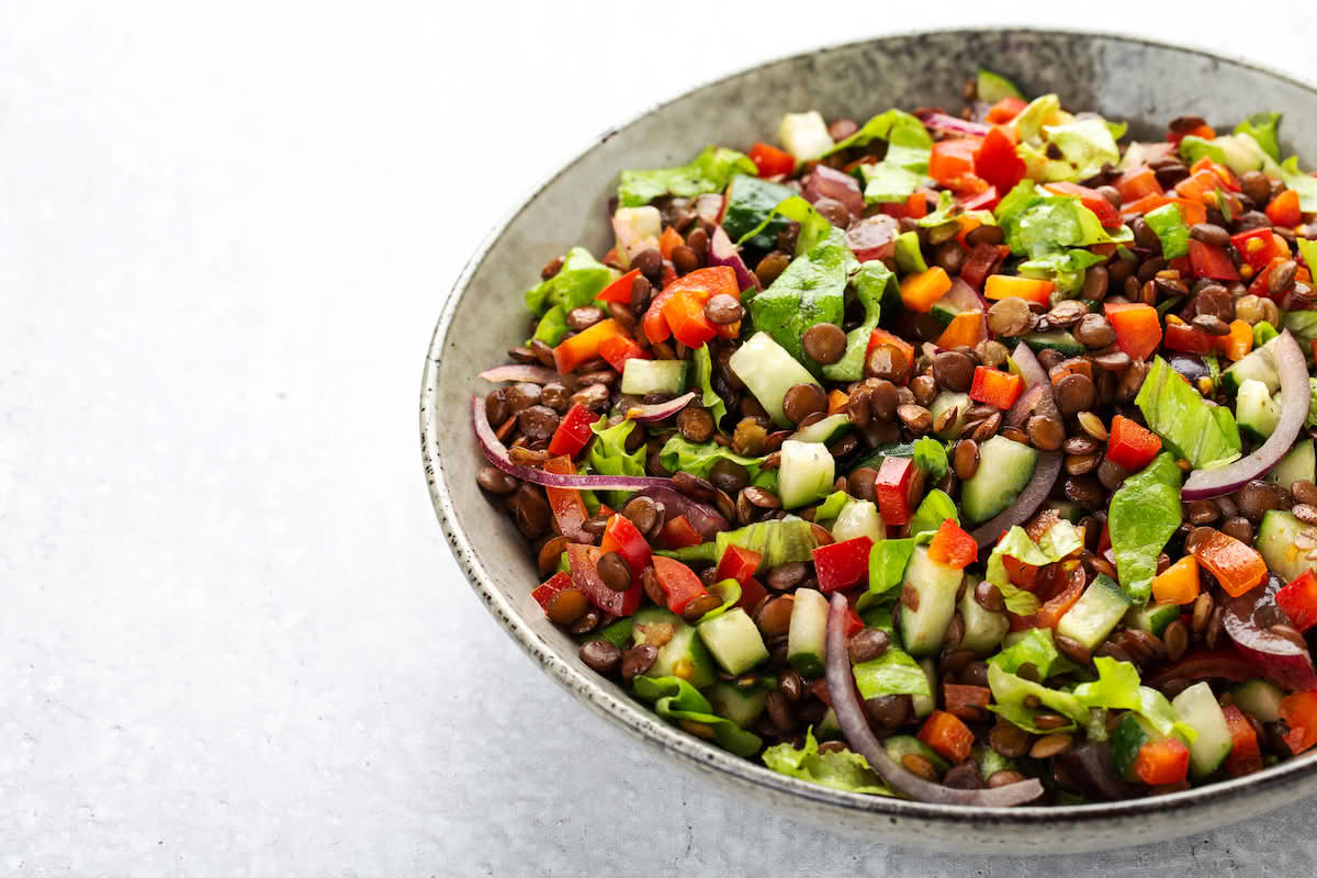 Skål med salat, linser, agurk, paprika og lauk. 