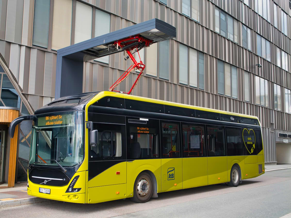 En gulgrønn buss med en metallkran over seg.