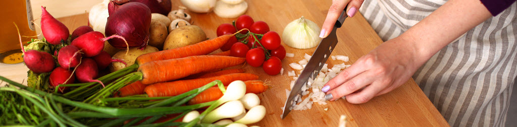 A woman chopping onions on a cutting board filled with fresh colorful vegetables