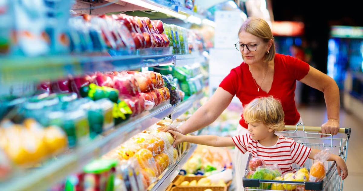 Shopping with kids. Mother and child buying fruit in supermarket. Mom and little boy buy fresh mango in grocery store. Family in shop. Parent and children in a mall choosing vegetables. Healthy food.