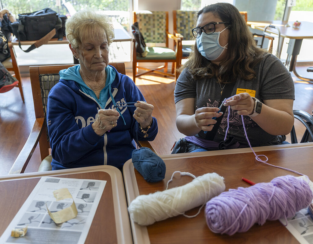 Two people sit side by side with crochet hooks and yarn.