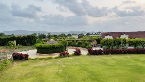 View across a lawn of a resort. Large circular feature in the center, like for driving around. Long view has mountains on the horizon.
