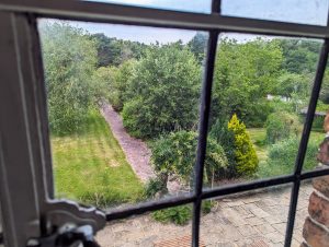 The view of a garden outside one of the Heskin Hall windows, an old manor house in North England. The photo includes some of the old metal window frame and glass.
