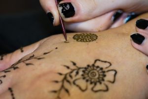 Artist painting mehndi floral motives with henna on a woman's hand