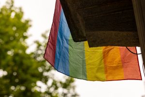 Bottom of a wrinkled pride flag  hanging from a balcony with a tree in the background