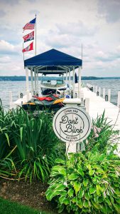 Single white pier with motorboat under a blue tent and a jetski in the foreground with a sign saying "Don't Blink" (Fontana-On-Geneva Lake, Wisconsin)