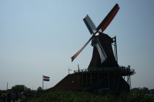 De Zoeker windmill in Zaanse Schans on a clear sunny day. Next to the windmill is the Dutch flag.