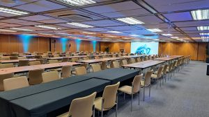 A spacious conference room is set up with multiple rows of tables and chairs.