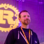 Jon Bauman standing in front of Rust logo projected on stone wall.