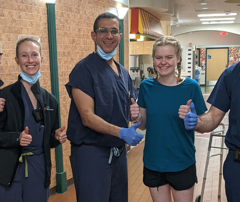 A group of four healthcare professionals and a patient stand in a hallway, all giving a thumbs-up gesture.