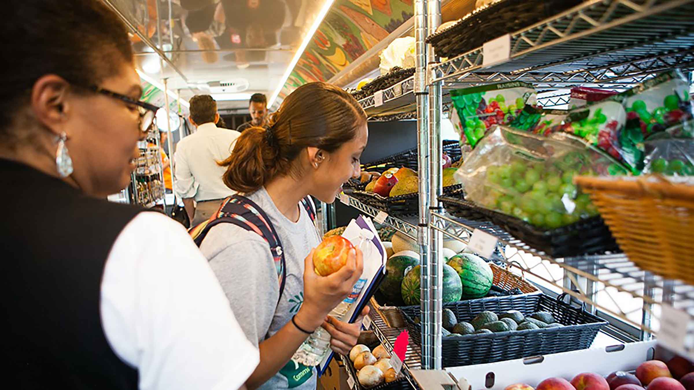 A group of people stand in front of a shelf filled with produce