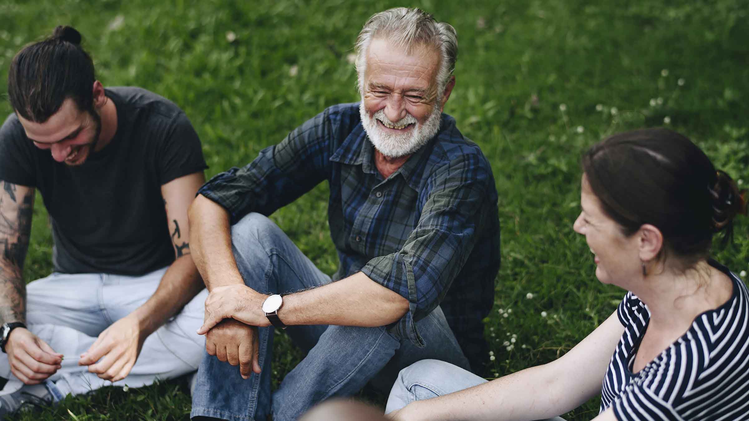 A group of adults sit together laughing in the grass at a park