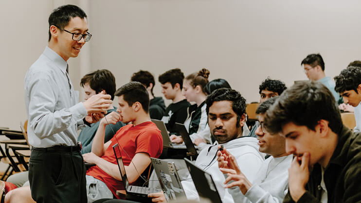Student answering a question in class while professor pays attention.