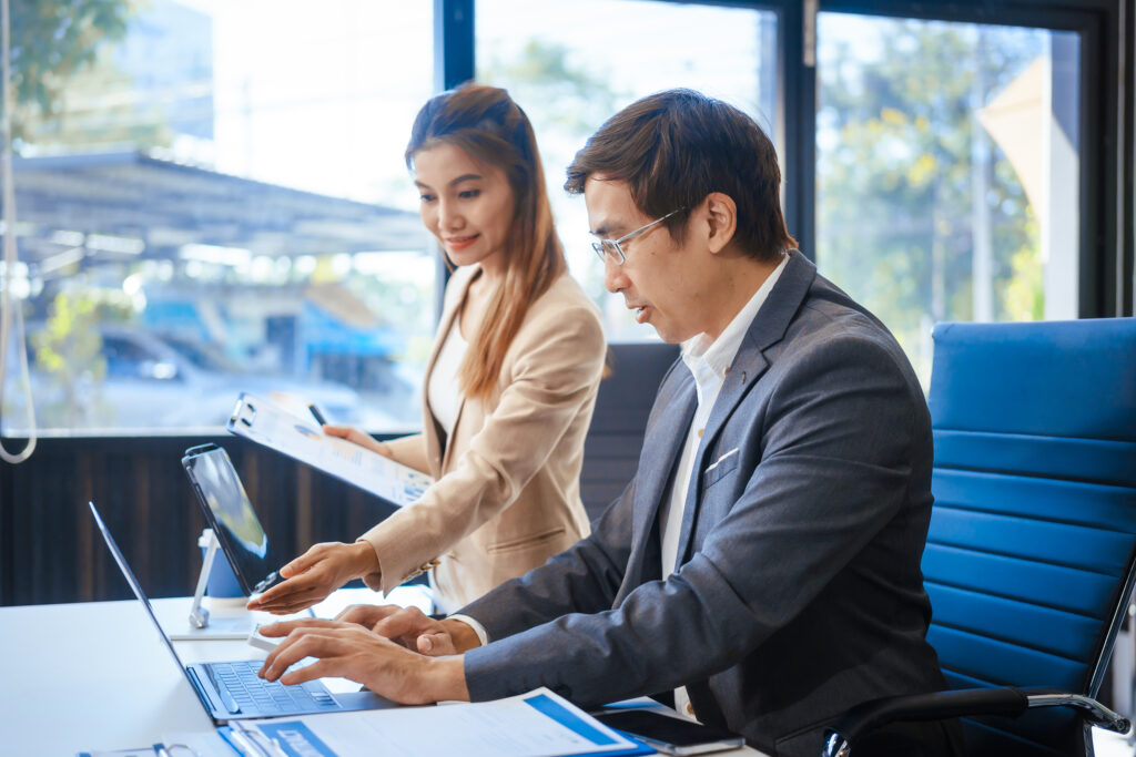 A businessman and woman sit at a modern office table, smiling di