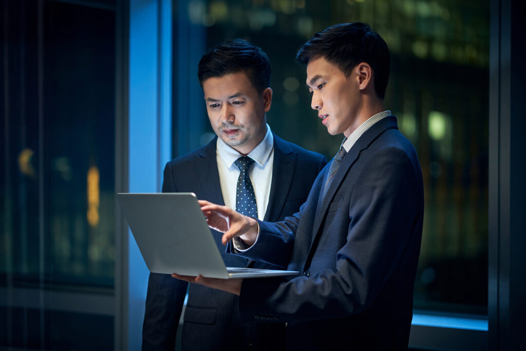 Two,Asian,Corporate,Executives,Standing,By,The,Window,In,Office