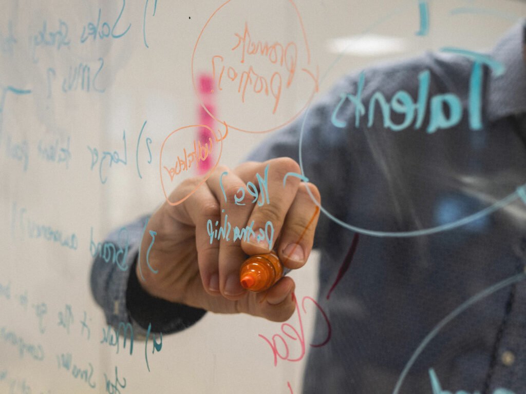 person writing on a clear board with a marker pen