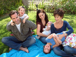 Mum holding baby while dad and grandma play with two older daughters on picnic blanket