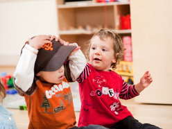 Toddler trying to grab her playmate's hat off his head