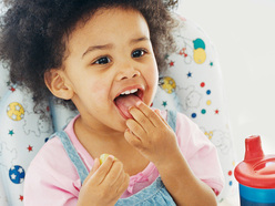 Little girl eating healthy food at highchair