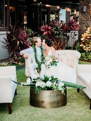 A joyful couple shares a tender moment on a lush lawn, surrounded by vibrant plants and elegant decor, capturing a celebration of love.